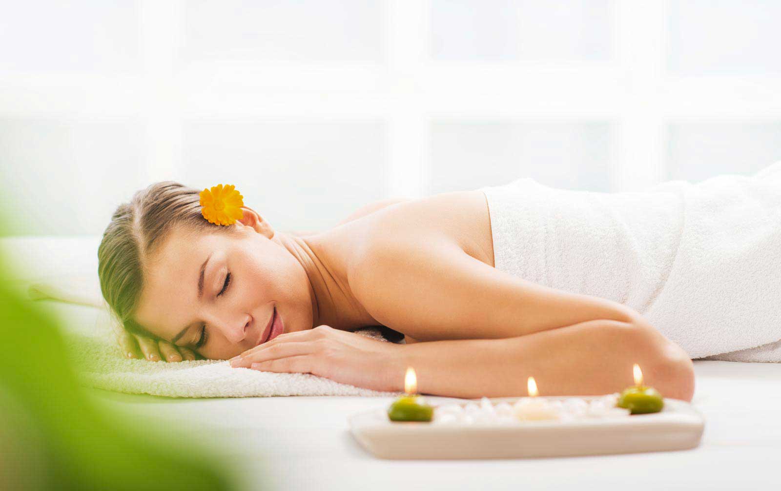 A woman relaxing with a flower in her hair during a spa treatment.