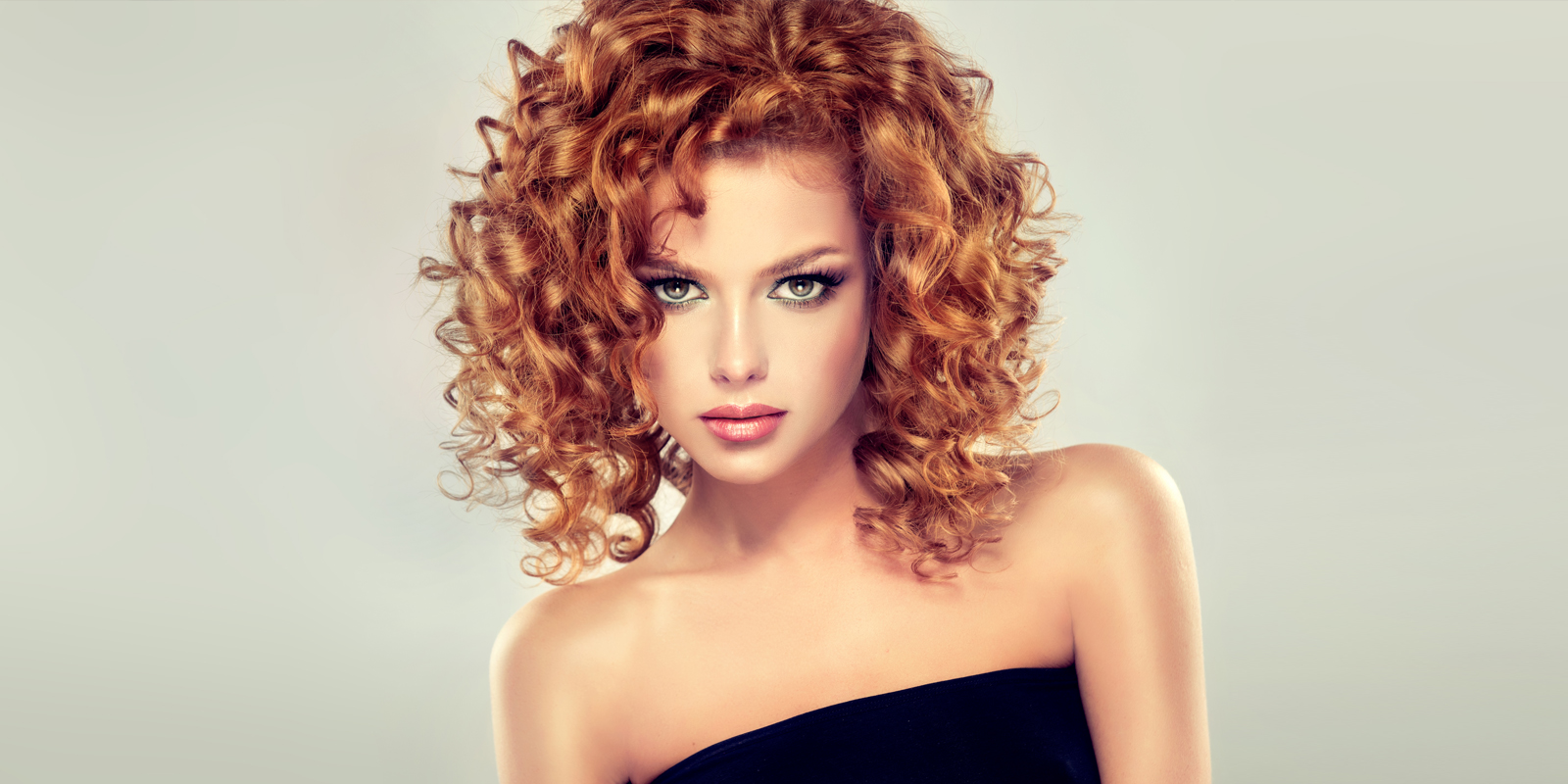 Portrait of a woman with curly red hair and striking makeup.