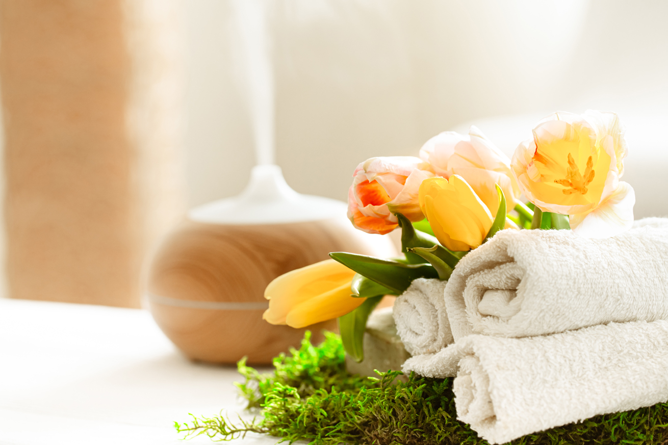 Aromatherapy diffuser with steam and fresh flowers beside rolled towels. Aromatherapy diffuser with steam and fresh flowers beside rolled towels.