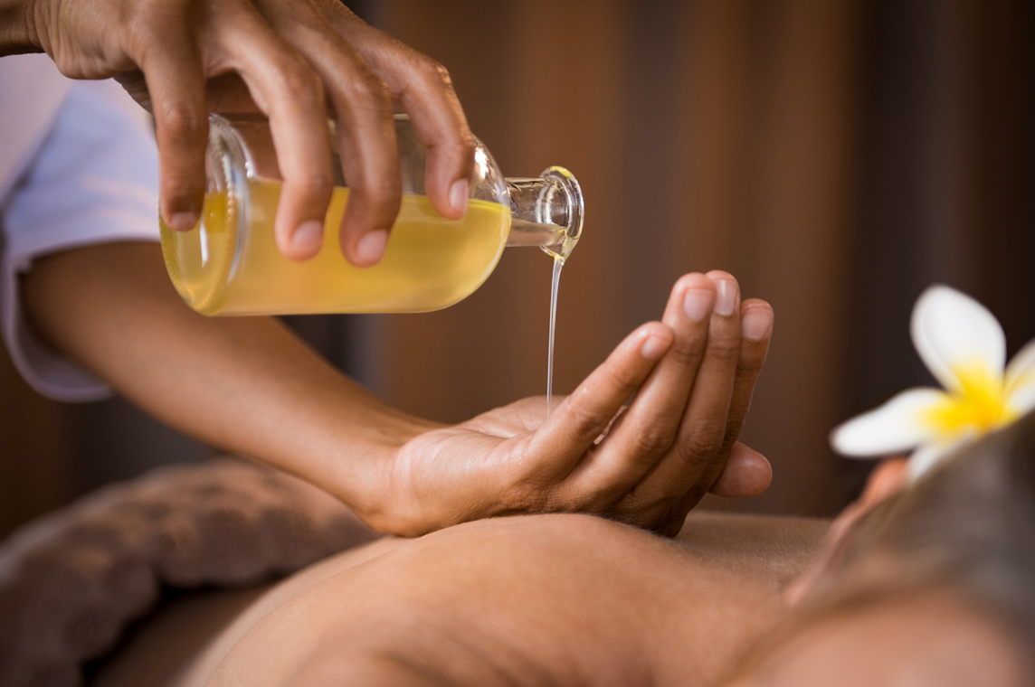 A person pouring massage oil onto another's back for a relaxing massage. A person pouring massage oil onto another's back for a relaxing massage.
