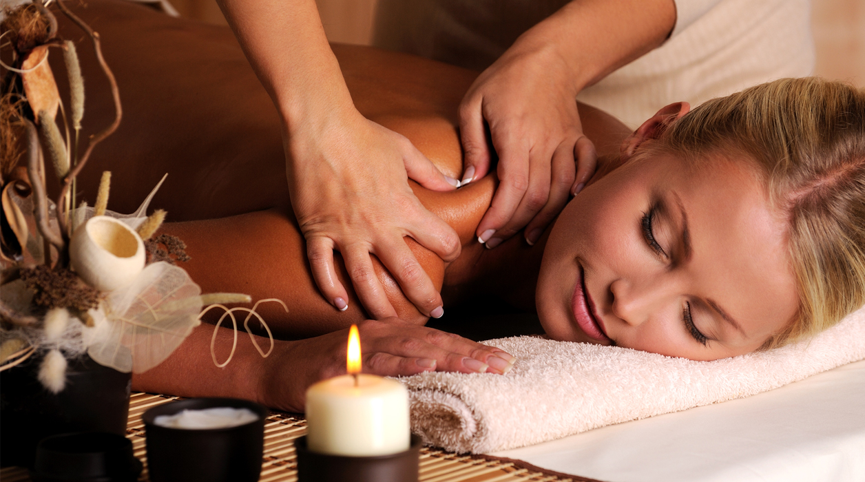 A person receiving a relaxing shoulder massage with a lit candle nearby. A person receiving a relaxing shoulder massage with a lit candle nearby.